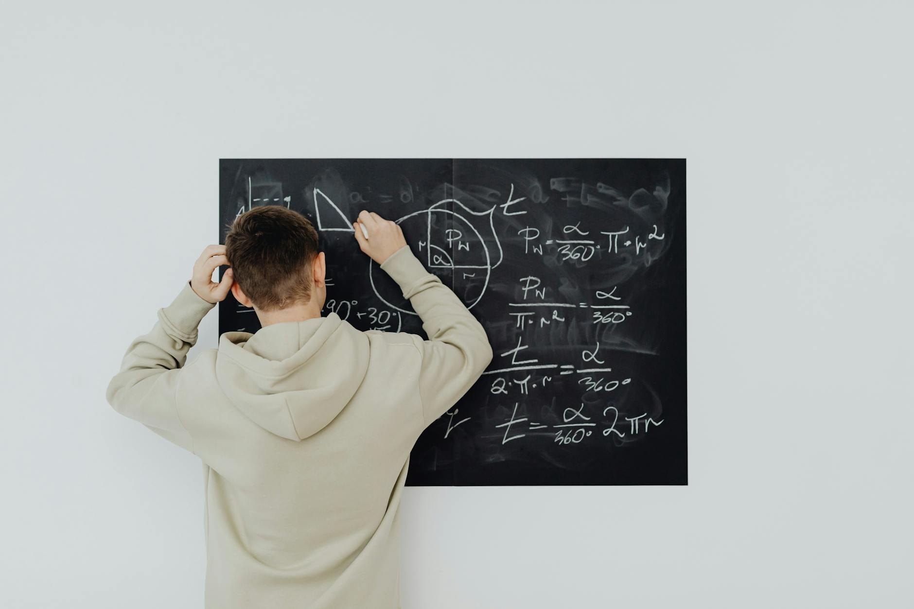 Uczeń w bluzie zapisuje wzory matematyczne na szkolnej tablicy